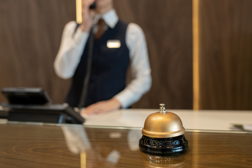bell-wooden-reception-counter-against-female-receptionist-consulting-clients-phone-while-working-contemporary-luxurious-hotel